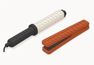 A curling iron with a charcoal handle, a white barrel and a short cord beside a terracotta flat iron with its plates closed.